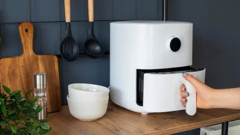 Bijela friteza na vrući zrak na drvenoj kuhinjskoj radnoj ploči.