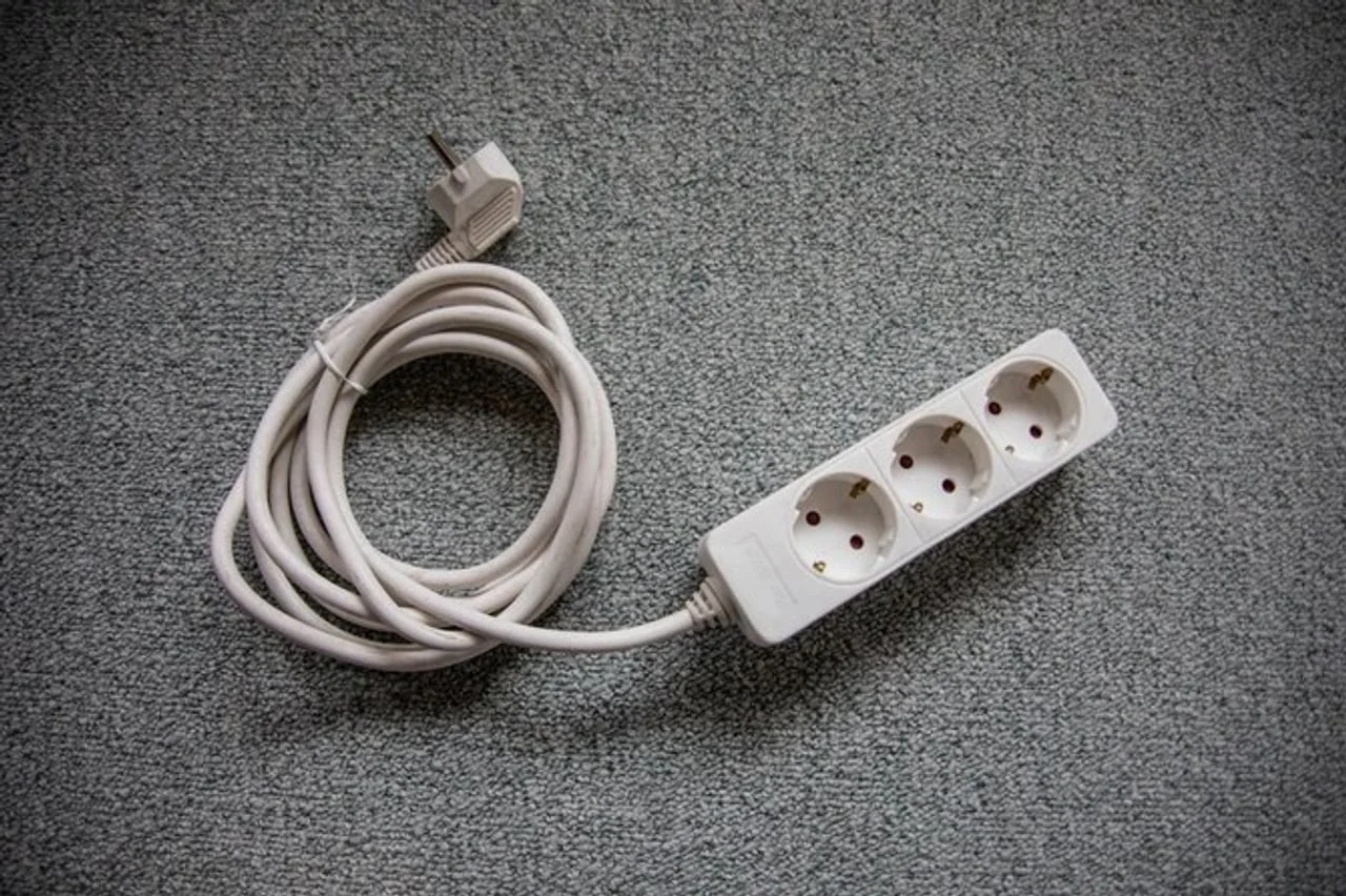 Bijeli produžni kabel s tri utičnice i zamotanim kabelom na sivoj podlozi