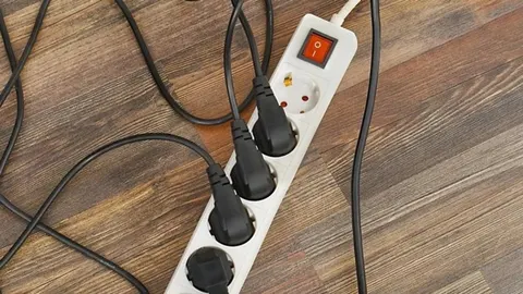 Bijeli produžni kabel s nekoliko utкнуutih crnih utikača na drvenom podu