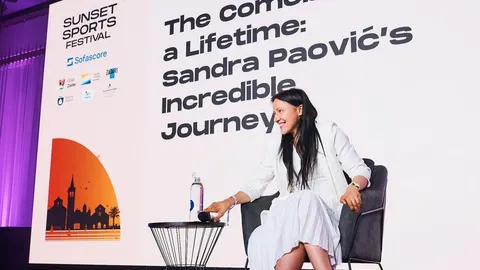 Sandra Paović u bijelom odelu sedi u fotelji ispred ekrana s napisom