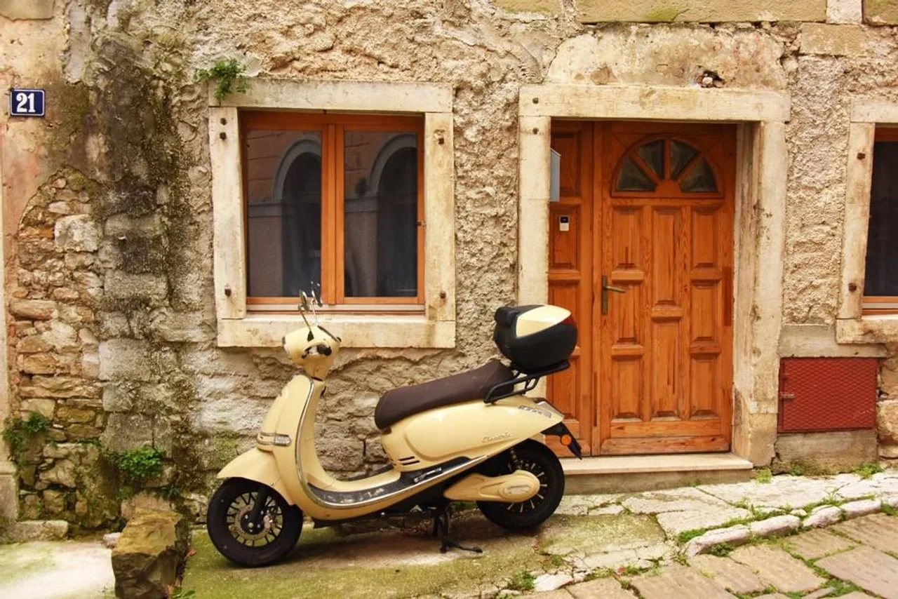 Svijetložuti skuter parkiran ispred stare kamene kuće s drvenim vratima.