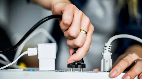 Ruka koja uključuje električni utikač u bijeli produžni kabel