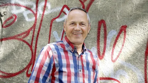 Osmijao muškarac srednjih godina u kariranoj košulji ispred grafitiranog zida
