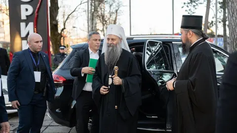Patrijarh Porfirije u crnom odjeću i bijeloj kapi stoji pored crnog automobila