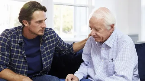 Mlađi muškarac pruža podršku starijoj osobi na kauču