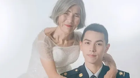 Starija žena u bijeloj vjenčanici grli mladog čovjeka u uniformi