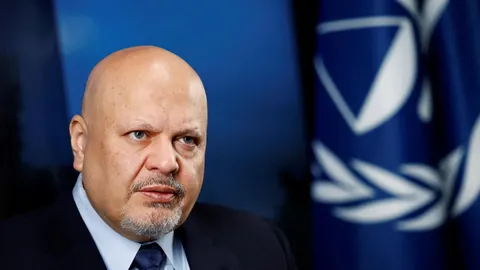 Portret Karima Khana u tamnom odelu ispred plave zastave