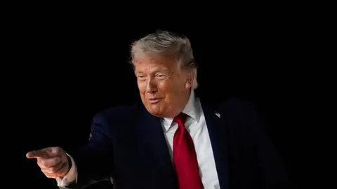 Donald Trump u tamnom odijelu i crvenoj kravati pokazuje prstom