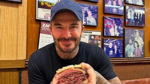 David Beckham u plavom kapu drži veliki sendvič s mesom