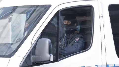 Policajac u crnoj opremi i maski za lice u bijelom službenom vozilu