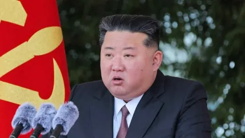 Portret Kim Jong Una u tamnom odelu ispred crvene zastave