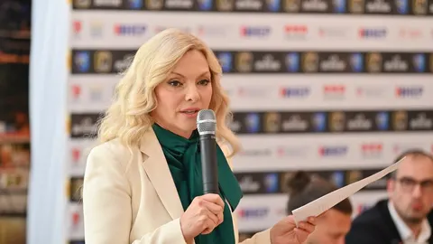 Vlatka Pokos drži mikrofon i papir pred pozadinom s logotipima
