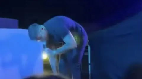 Muškarac u tamnoj odjeći nagnut prema dolje na osvjetljenoj pozornici