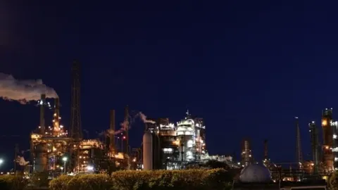 Noćni prikaz industrijske rafinerije s osvijetljenim towerima i dimnjakima