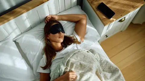 Žena spava u krevetu s maskom za spavanje preko očiju