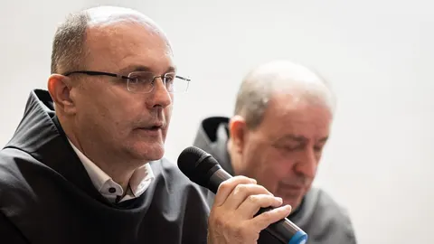 Srednje star muškarac u crnom svećeničkom habitu s naočalama govori u mikrofon
