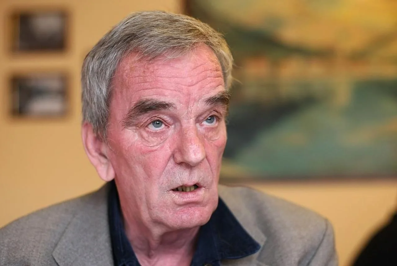 Portret starijeg muškarca s sijivom kosom u sivom sako i plavoj košulji