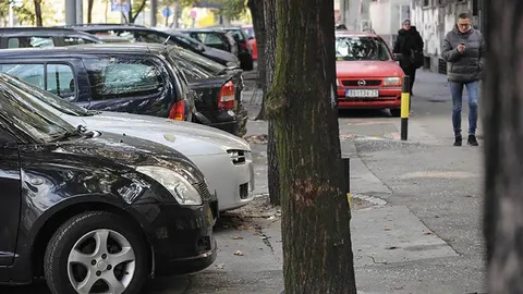 Redak parkednih automobila uz ulicu s drvima i prolaznikom
