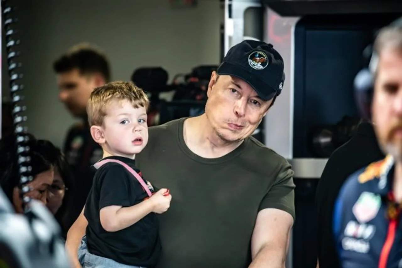 Elon Musk u crnoj kapi drži male dijete u naručju