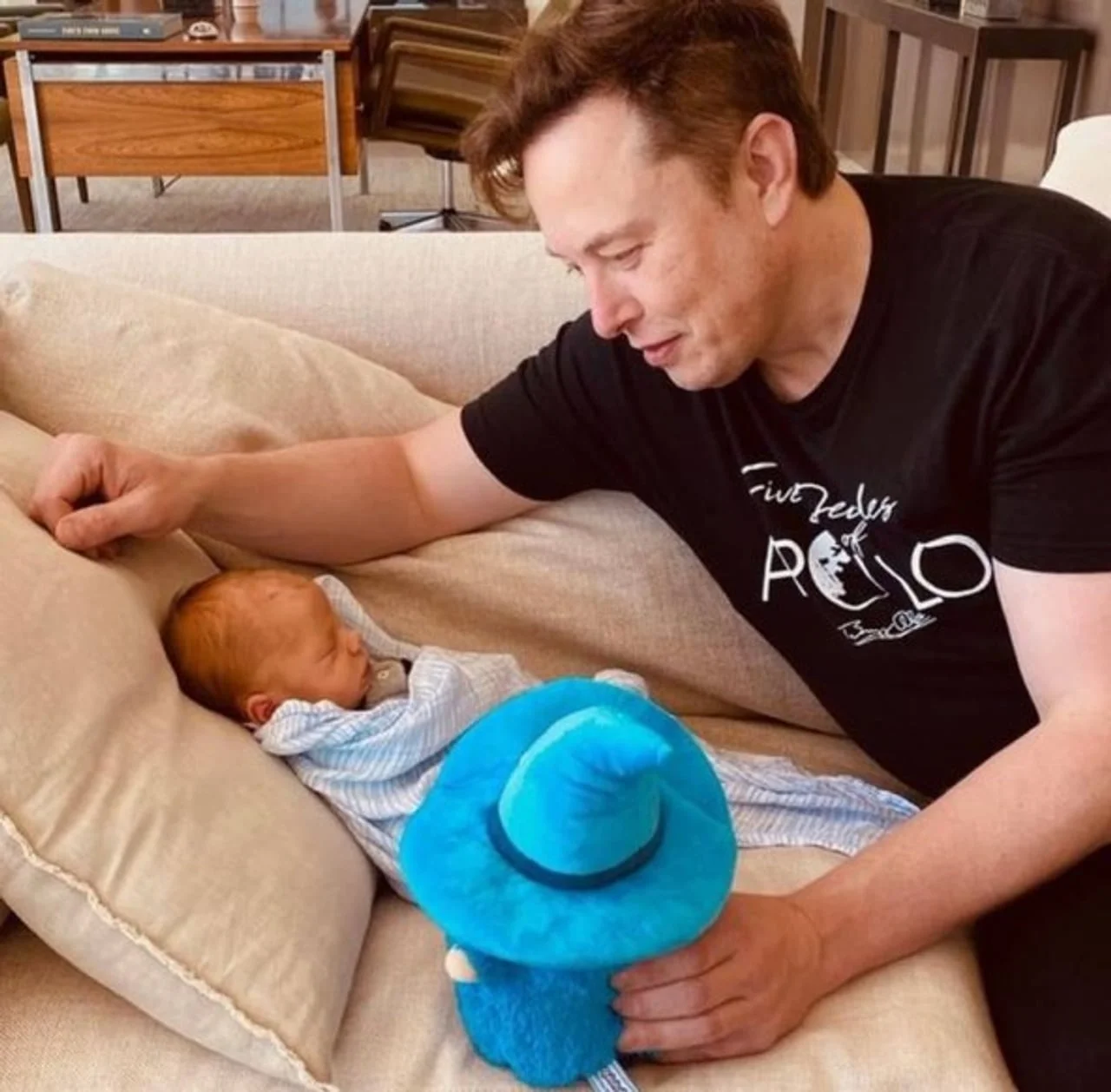 Elon Musk u crnoj majici gleda u novorođenče na kauču