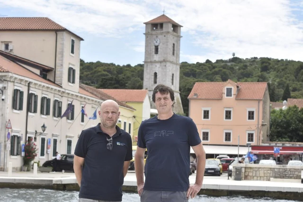 Dva muškarca pred zgradama i crkvbenim tornjem