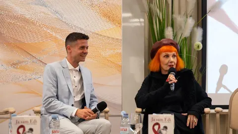 Muškarac u svijetlom odelu i žena s narandžastom kosom razgovaraju u studia