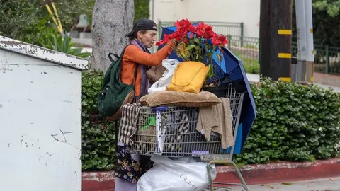 Žena u narandžastoj jakni pored pune shopping kolica s cvijećem