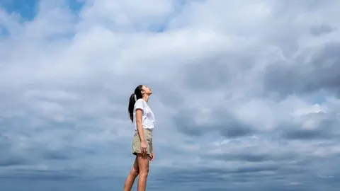 Žena u bijeloj majici stoji na otvorenom i gleda prema oblacima