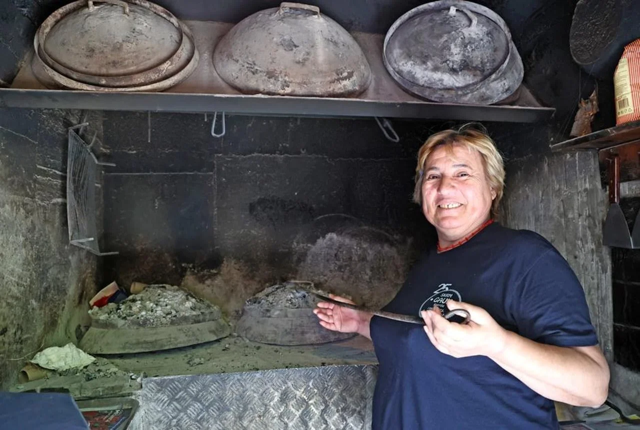 Žena u plavoj majici stoji ispred tradicionalne peći za pečenje