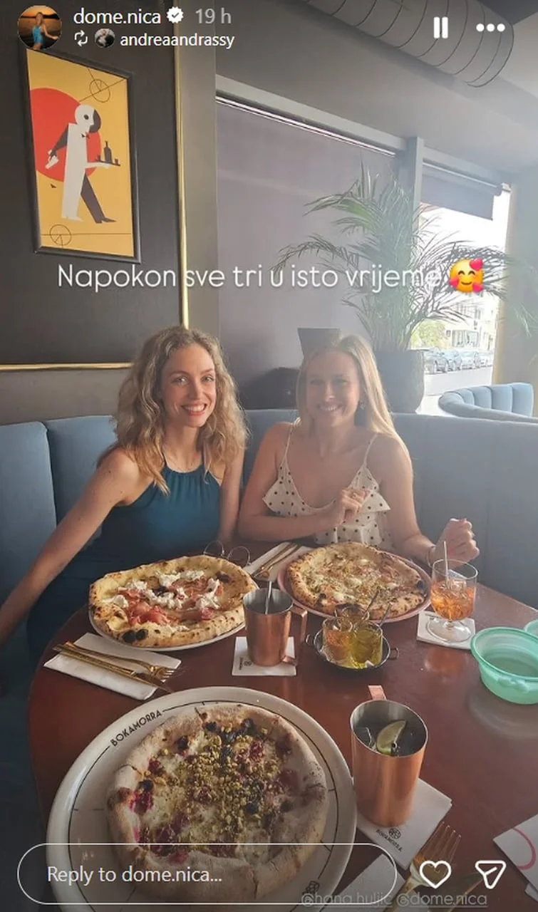 Dvije žene sjede za stolom s tri različite pizze i pićima