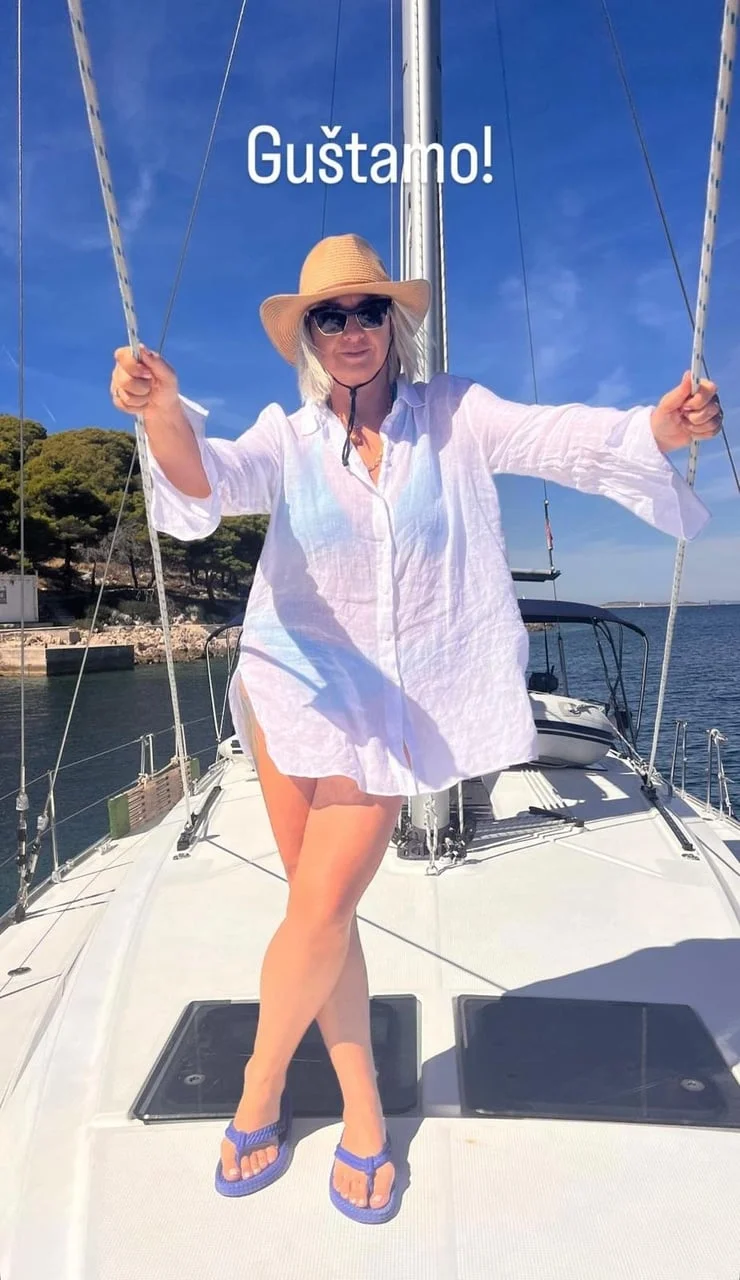 Žena u bijeloj košulji, šeširu i sunčanim naočalama na jedrilici