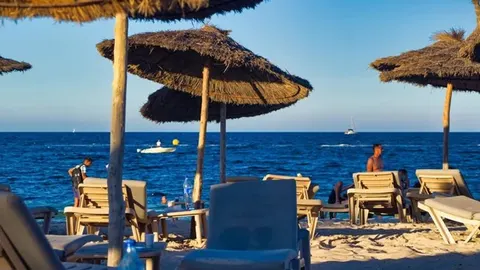 Pješčana plaža s drvenim suncobrima i ležaljkama uz plavo more