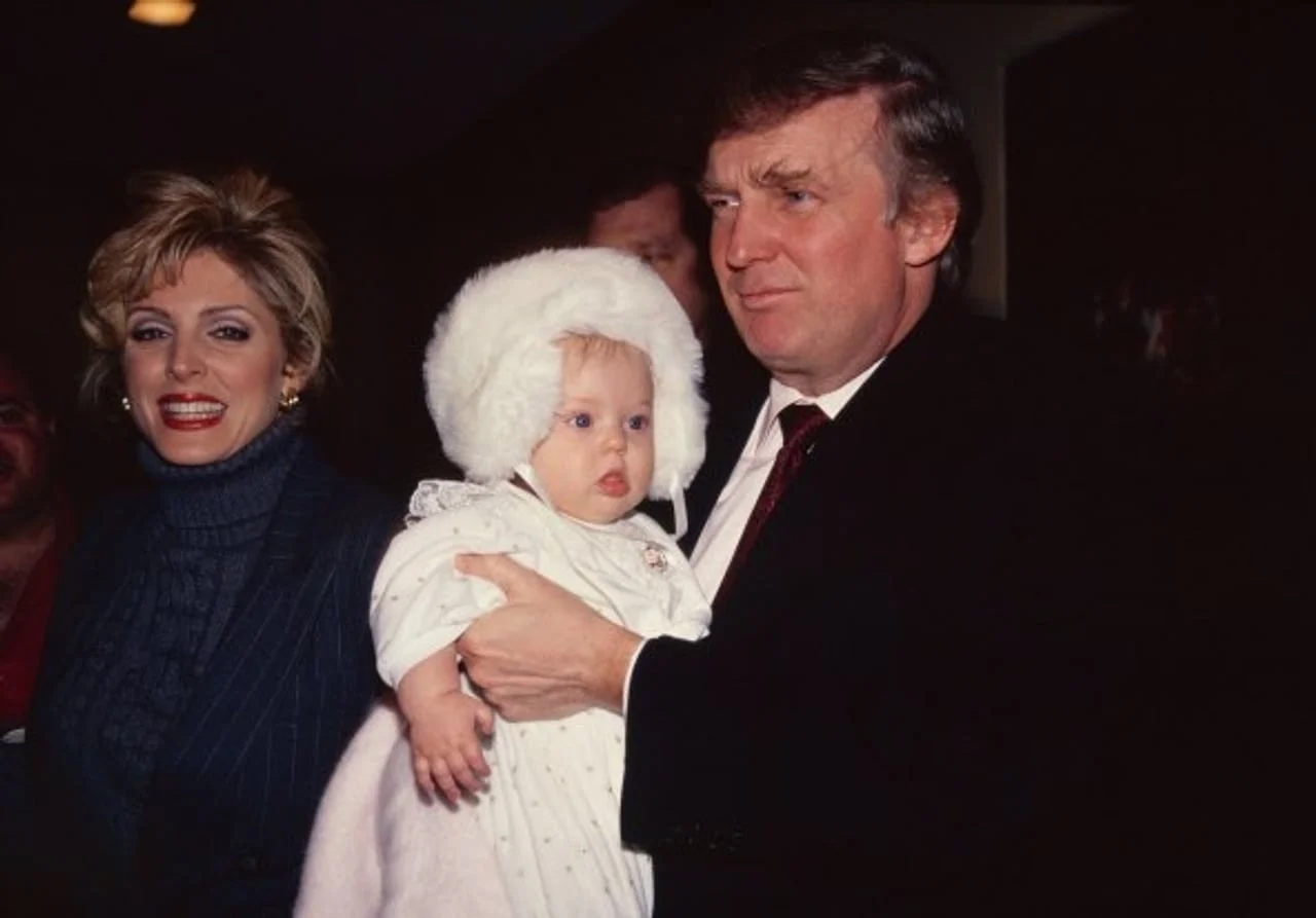 Donald Trump koji drži bebu u beloj kapuljači pored žene