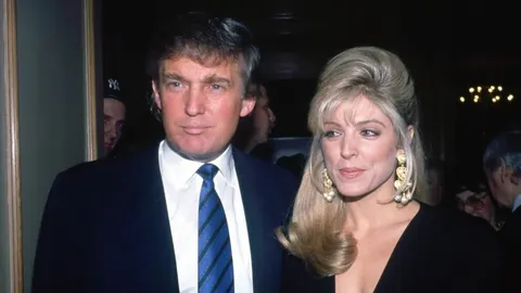 Mlađi Donald Trump u odelu i plavoj kravati pored žene plave kose