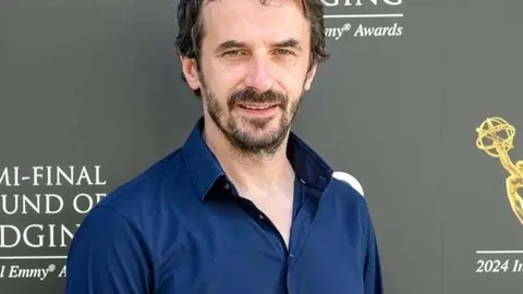 Portret glumca Igora Kovača u plavoj košulji ispred pozadine s natpisima