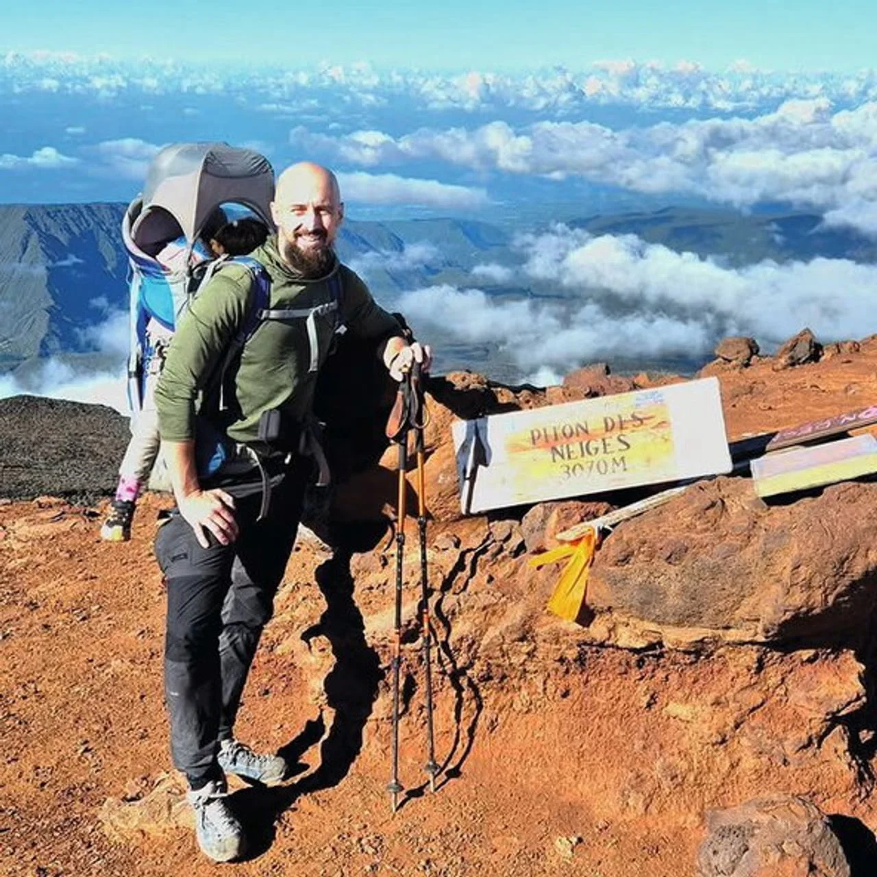 Muškarac s djetetom pored natpisa Piton des Neiges 3070m na crvenom tlu