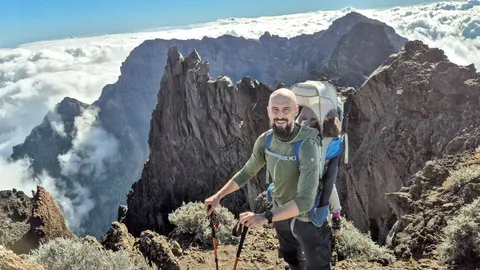Muškarac s djetetom u nosnjici na vrhu stjenovite planine iznad oblaka