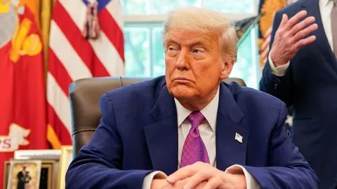 Donald Trump u plavom odelu i ljubičastoj kravati sedi u uredu