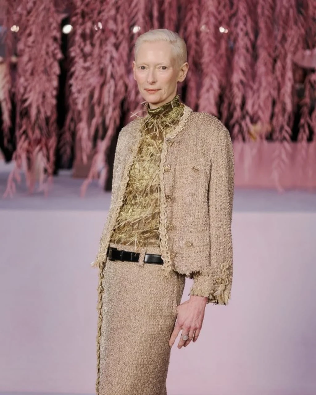Tilda Swinton u elegantnom bež odjelu pred roza pozadinom