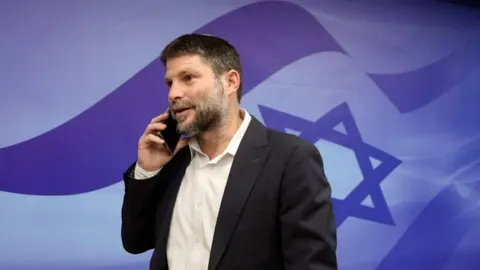 Izraelski ministar Bezalel Smotrich razgovara telefonom ispred zastave Izraela