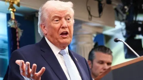 Donald Trump u tamnom odijelu i svijetloj kravati govori za govornicom
