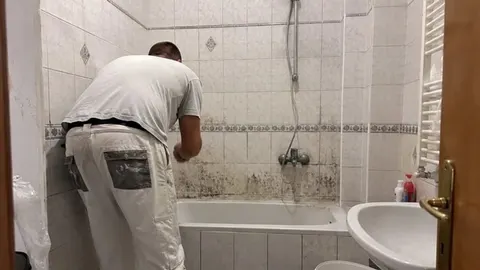 Čovjek u radnim hlačama čisti plijesan s pločica u kupaonici