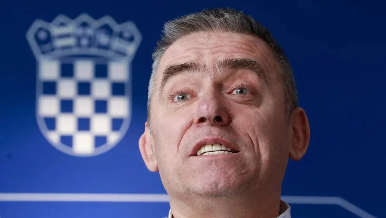 Krupni plan lica muškarca ispred plave pozadine s grbom