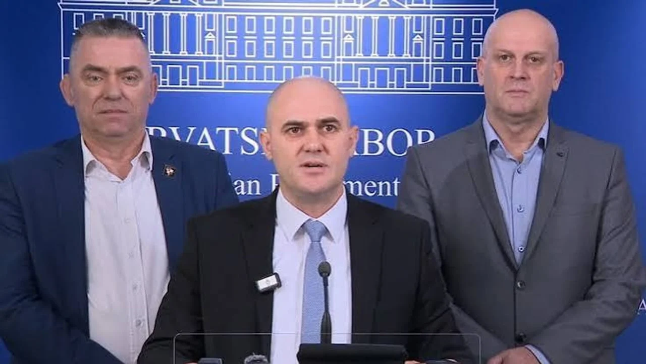 Troje muškaraca u odijelima ispred plave pozadine s natpisom