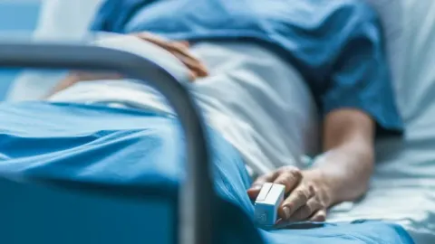 Pacijent leži u bolničkom krevetu s pulsnim oksimetrom na prstu.