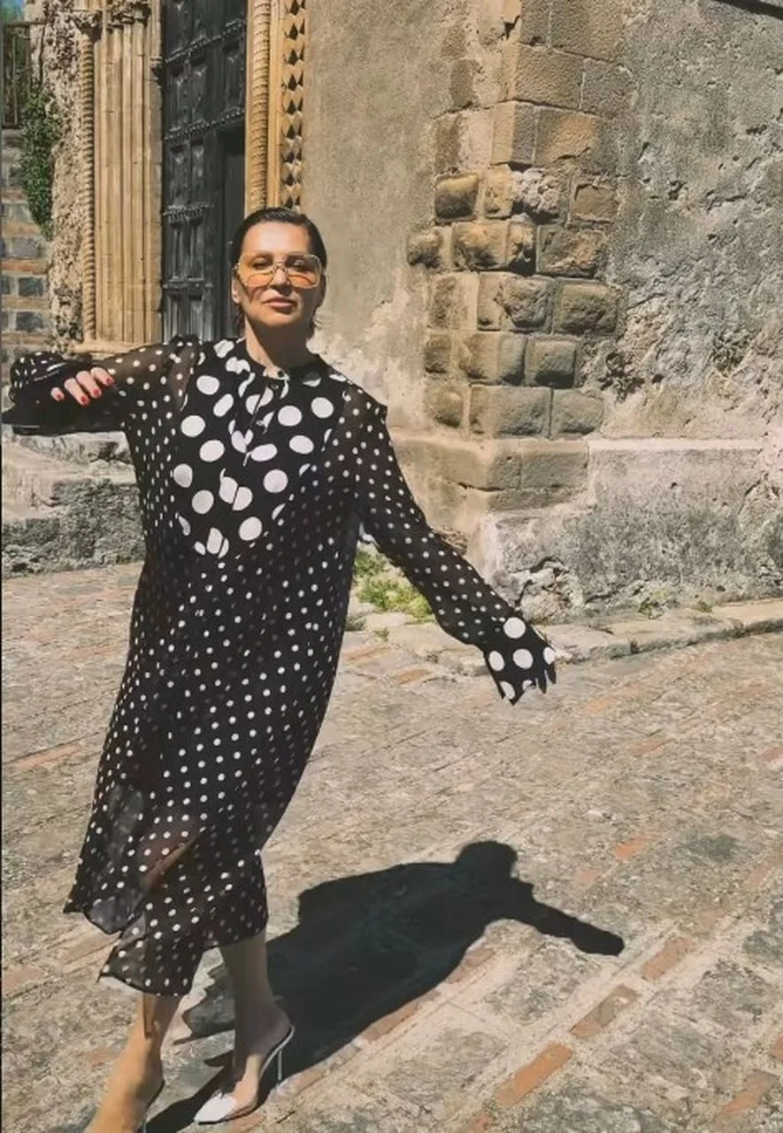 Žena u crnoj haljini na točkice ispred starog kamenog zida