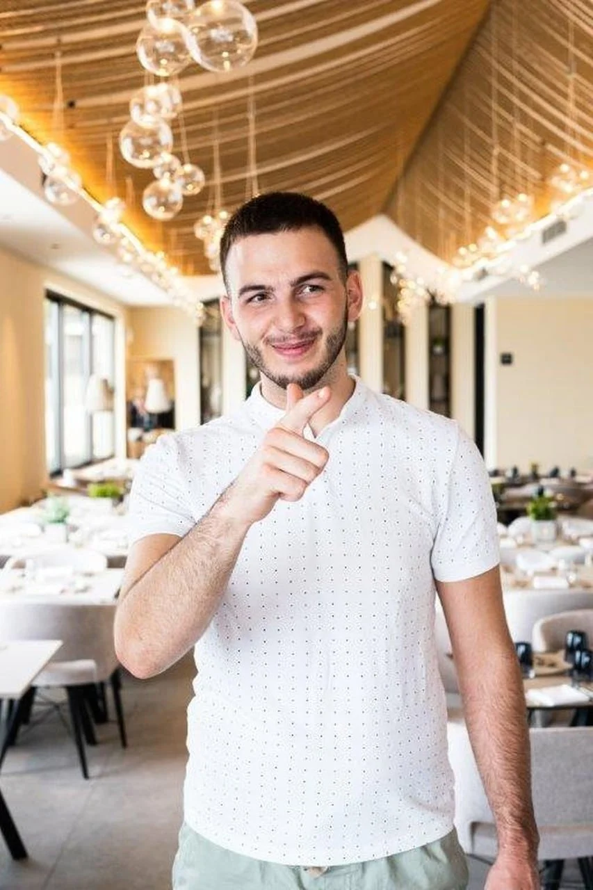 Muškarac u bijeloj polo majici stoji u modernom restoranu s dekorativnim svjetlima