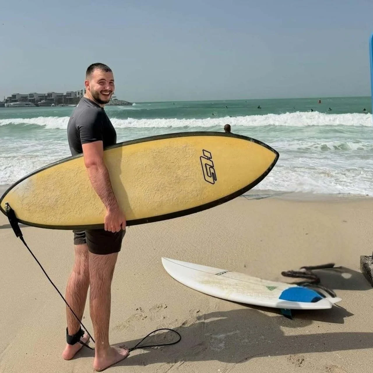 Muškarac na plaži drži dasku za surfanje uz obalu s valovima