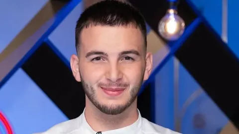 Portret mladog muškarca s kratkom kosom i bradom u bijeloj kuharskoj jakni