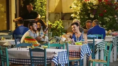 Ljudi sjede za stolovima u tradicionalnoj grčkoj taverni navečer